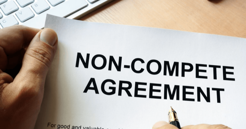 A man looks over a non-compete agreement with a pen in his hand, ready to sign.