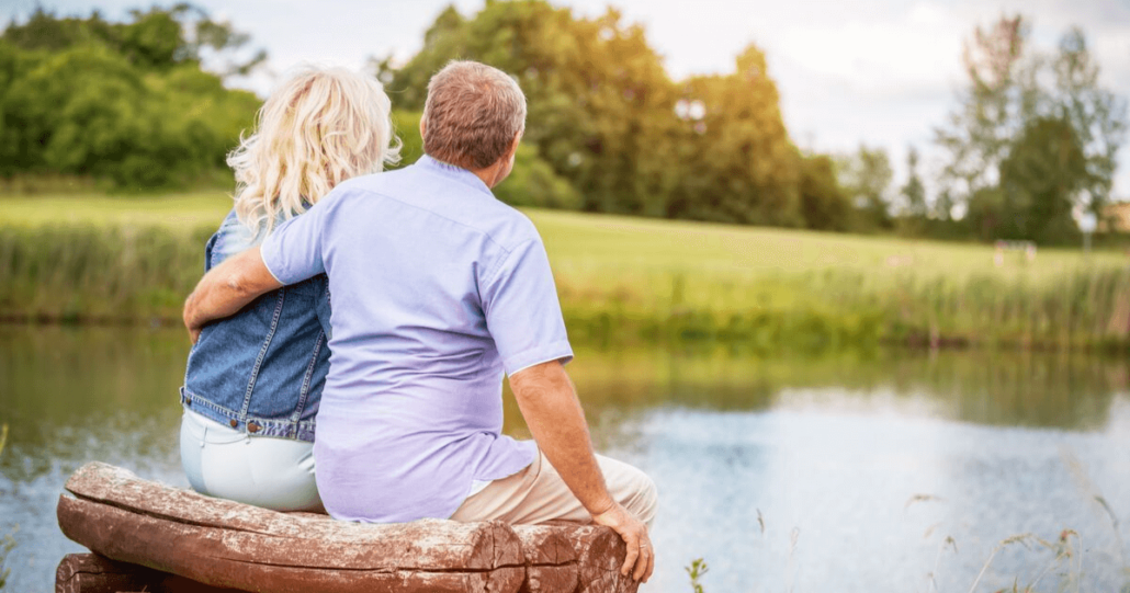 A couple in a common law marriage sit on a bench beside a pond
